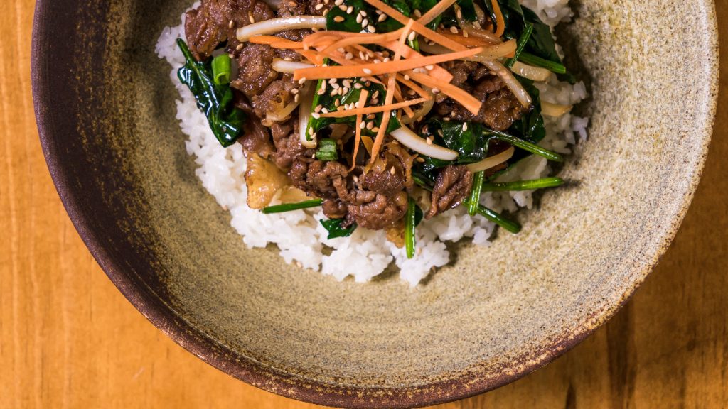 Korean rice bowl topped with beef, spinach, bean sprouts, carrot and sesame seeds.