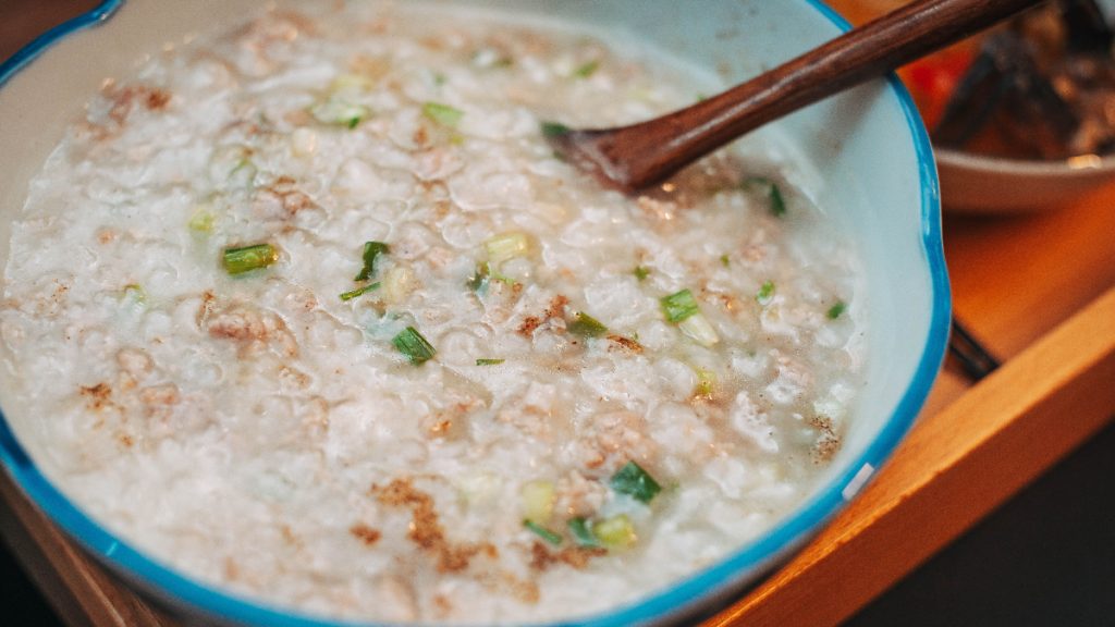 Bowl of savoury rice congee topped with chopped spring onions, with a wooden spoon resting inside.