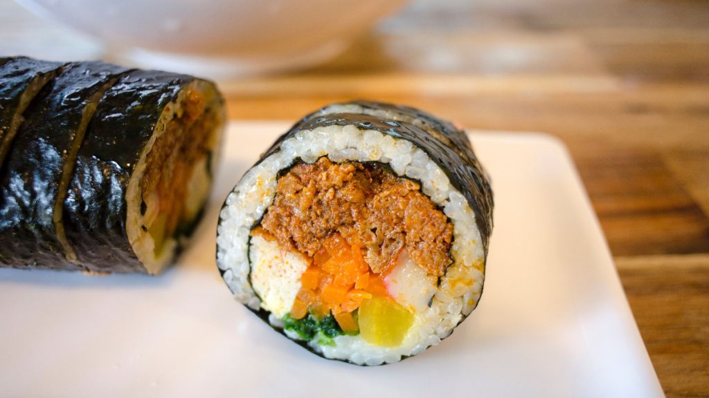 Close-up of sliced kimbap filled with rice, vegetables and assorted fillings, wrapped in seaweed.