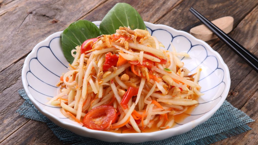 Thai som tam salad made with shredded green papaya, tomatoes, carrot, chillies and peanuts in a patterned bowl.