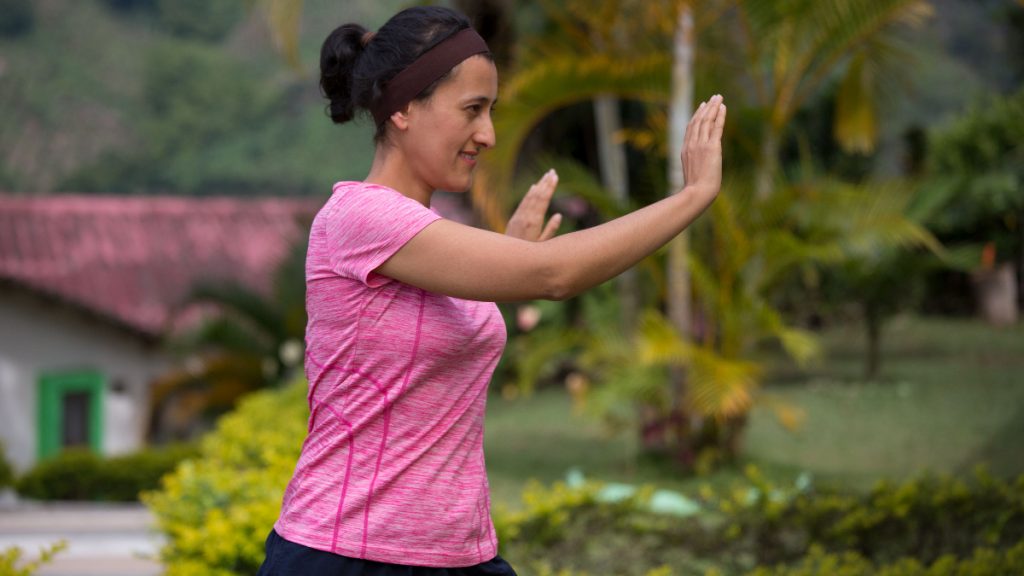 Woman practising a slow tai chi movement outdoors with one arm extended.